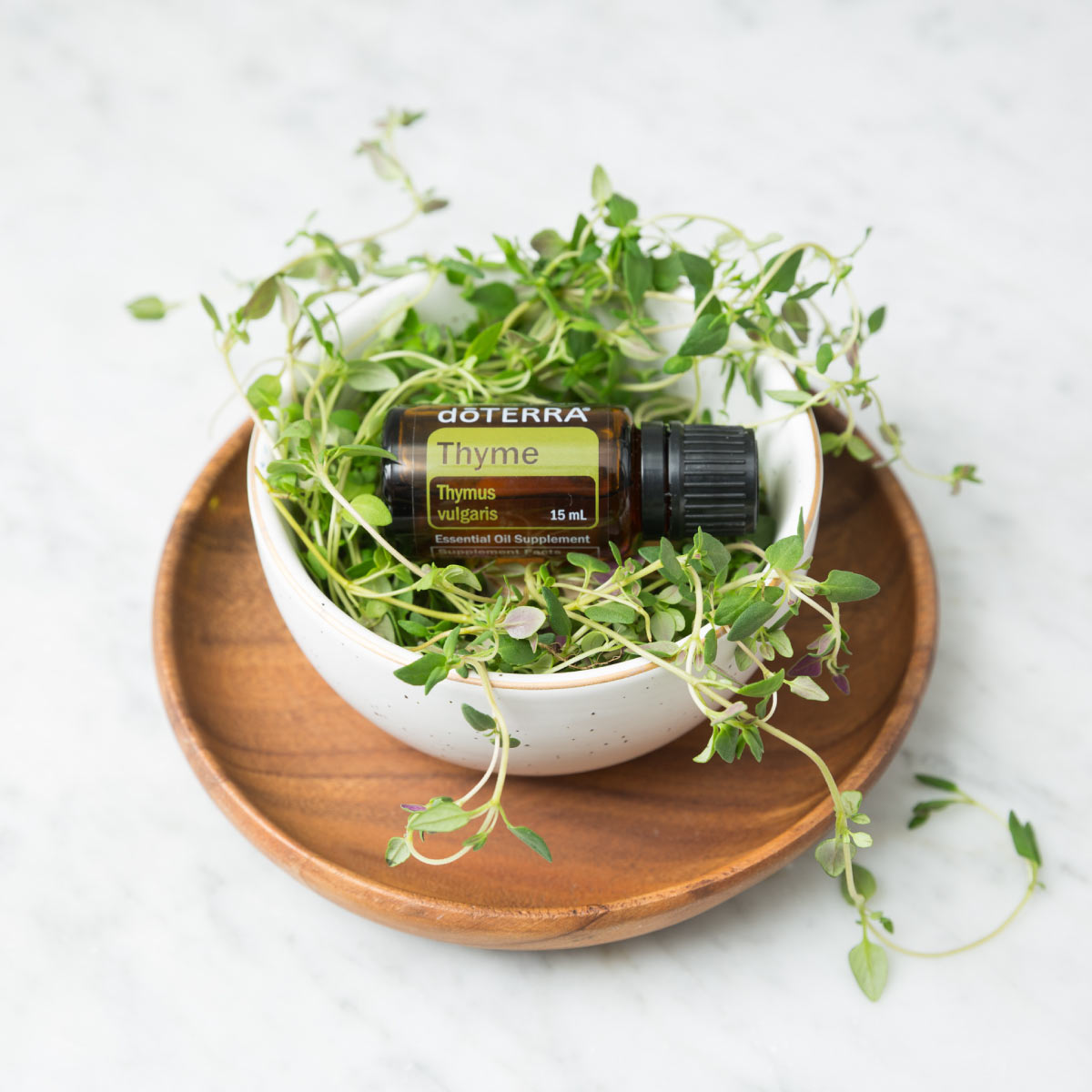 Bottle of Thyme oil surrounded by green leaves in a small white bowl sitting on a wooden dish. How do you use Thyme essential oil? You can use Thyme essential oil to promote a healthy immune system, to add flavor when cooking, or to repel insects. 