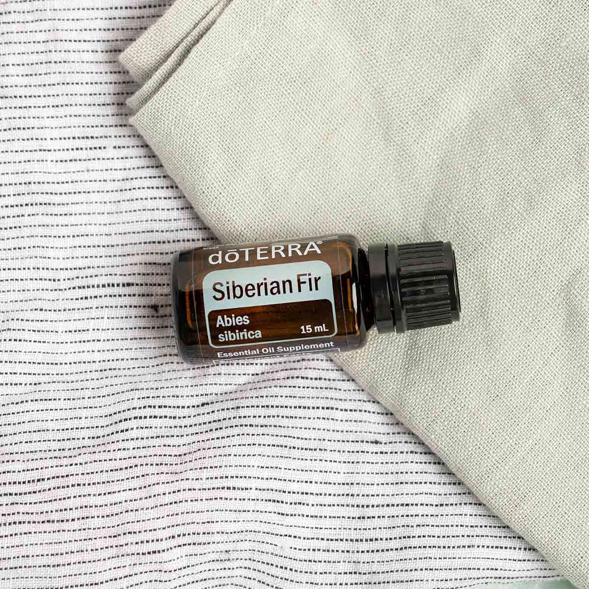 Bottle of Siberian Fir oil resting on a dish cloth. What are the benefits of Siberian Fir oil? Siberian Fir essential oil holds benefits for the ski